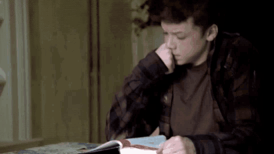 a young boy in a plaid shirt is reading a book