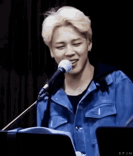 a young man in a blue jacket is singing into a microphone while sitting at a piano .