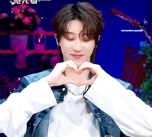a man is making a heart shape with his hands and the words strawberrymilk are visible behind him