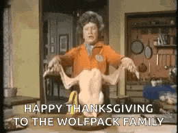 a woman is holding a dead chicken on a table and saying `` happy thanksgiving to the wolfpack family '' .
