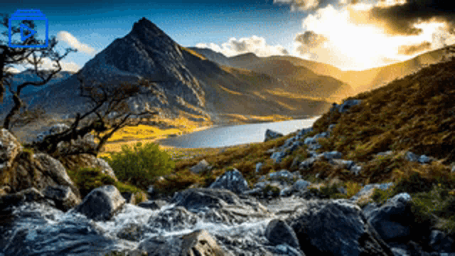a river runs through a valley with mountains in the background and the sun shining through the clouds behind it