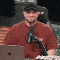 a man in a red shirt is sitting in front of a microphone in front of an apple laptop