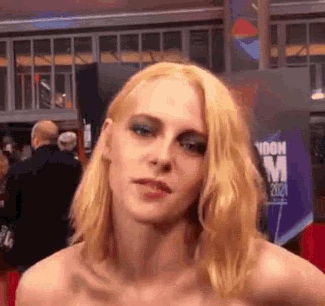 a woman with blonde hair and blue eyeshadow is standing on a red carpet in front of a building .