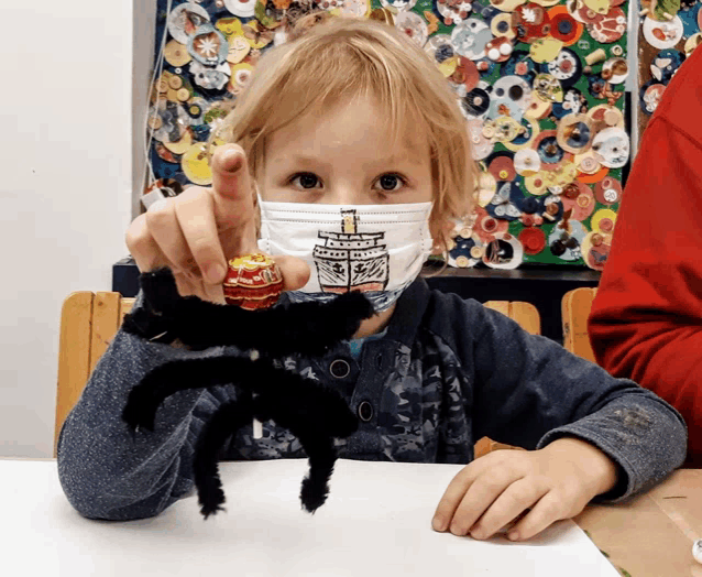 a young boy wearing a face mask is holding a black spider