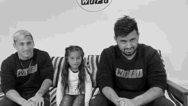 two men and a little girl are sitting on a couch wearing sweaters that say wtf