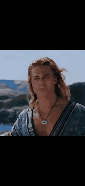 a man with long blonde hair is wearing a necklace and a blue shirt .