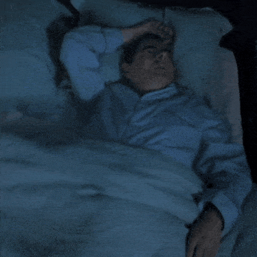 a man with a beard is sleeping in a bed with a remote control in his hand .