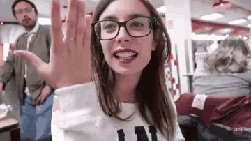 a woman wearing glasses and a white shirt with the letter l on it