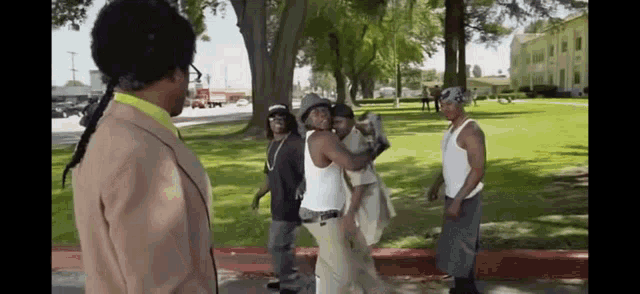 a group of men are standing on a sidewalk in a park talking to each other .