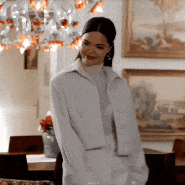 a woman in a white coat is smiling in a room with a painting on the wall