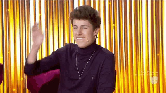 a young man is sitting in front of a gold curtain .
