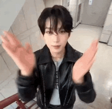 a young man in a leather jacket is standing next to a staircase with his hands outstretched .