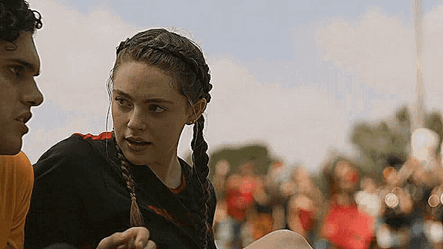a man and a woman are sitting next to each other on a field . the woman has braids in her hair .