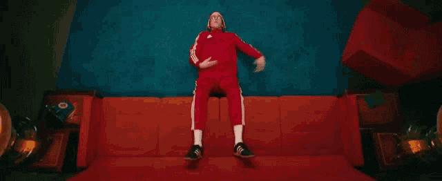 a man in a red jumpsuit is sitting on a red couch and dancing .
