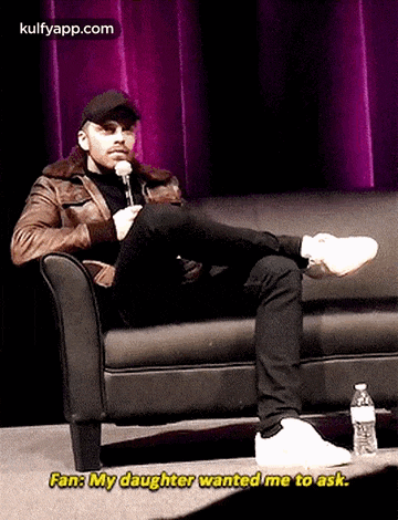 a man is sitting on a couch with his legs crossed and a microphone .