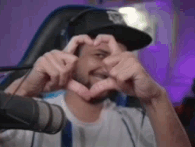a man in a baseball cap is making a heart shape with his hands .