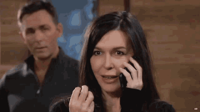a woman is talking on a cell phone with a man standing behind her .