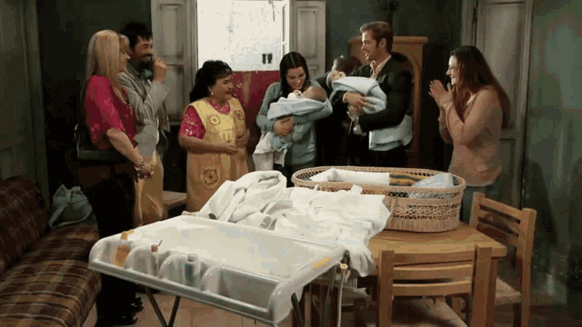 a group of people standing around a table with two babies in a crib