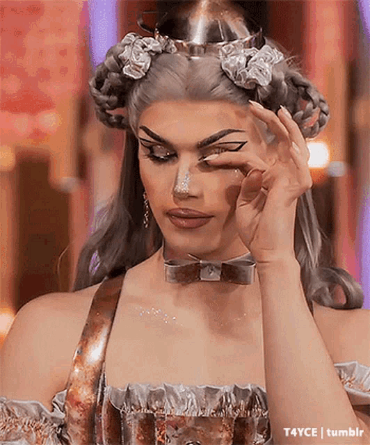 a drag queen is covering her eye with her hand while wearing a crown and a bow tie .