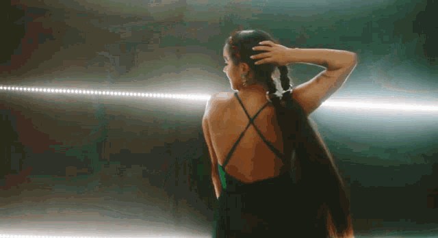 a woman in a green dress is standing in a dark room holding her hair in a ponytail .