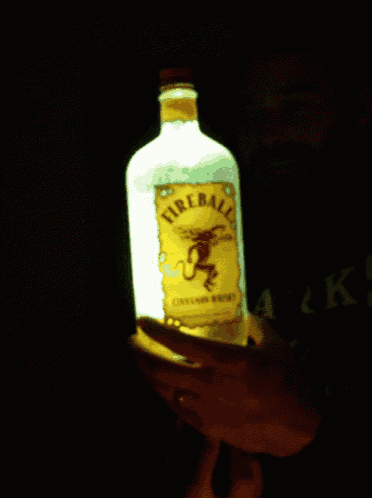 a person is holding a lit up bottle of fireball whiskey