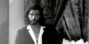 a black and white photo of a man with long hair and a beard wearing a suit and a white shirt .