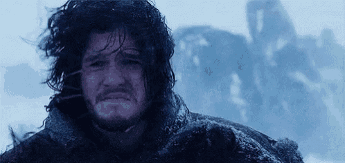 a man with long hair and a beard is standing in the snow with a castle in the background .