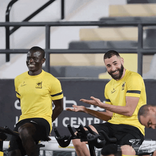 a man in a yellow nike shirt sits next to another man on a bike