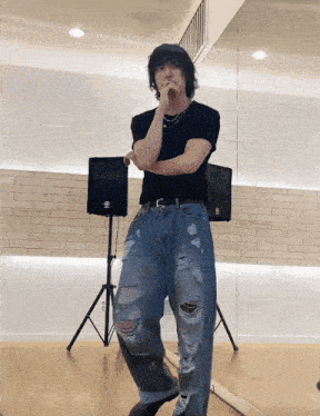a man in a black shirt and ripped jeans stands in front of a mirror