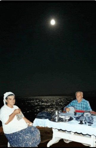 a man and a woman sit at a table with a full moon behind them