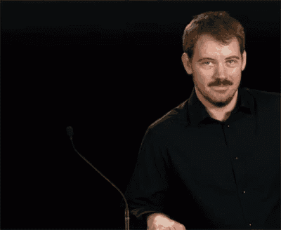 a man in a black shirt stands in front of a microphone and looks at the camera