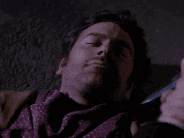 a man with a purple scarf around his neck is laying down with his eyes closed