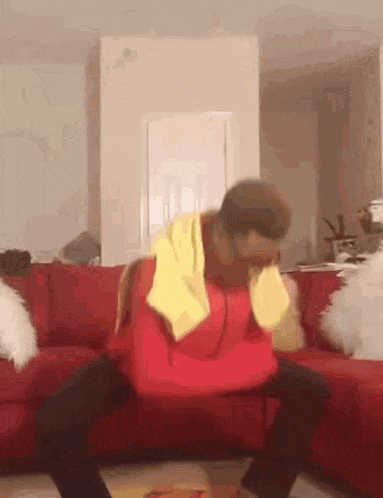 a man in a red hoodie is sitting on a red couch with his legs crossed .