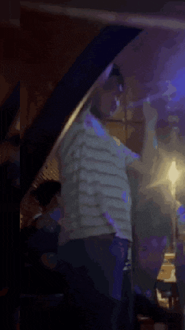 a man in a striped shirt is standing in a dark room with a purple light behind him