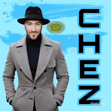 a man wearing a hat and a grey coat is standing in front of a blue background with the word uhen written on it