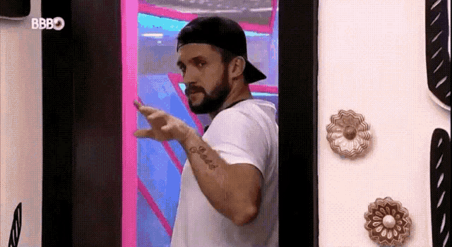 a man wearing a baseball cap and a white shirt is standing in front of a pink door .