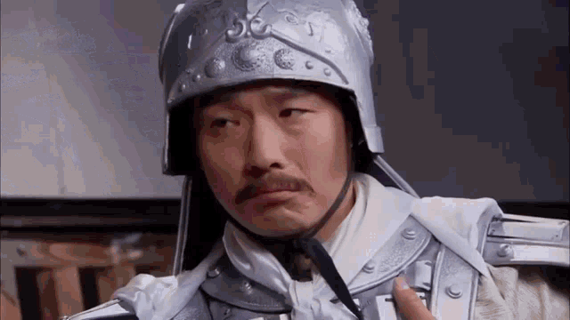 a man with a mustache is wearing a helmet and armor and making a funny face .
