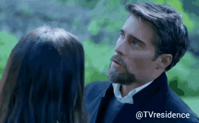 a man with a beard is looking at a woman with a green background .
