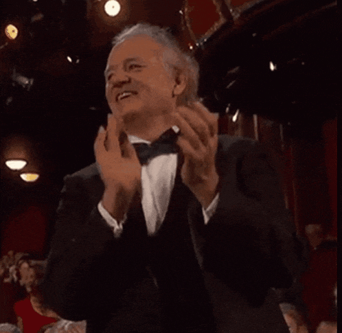 a man in a tuxedo and bow tie is applauding in a crowd of people .