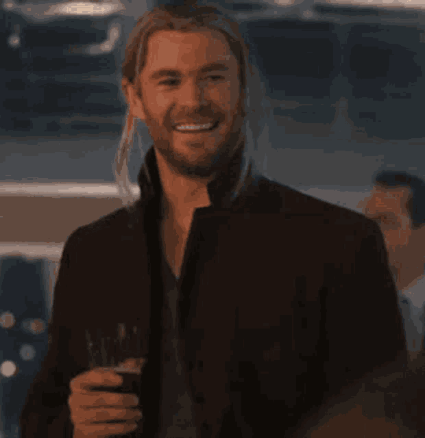 a man with long hair and a beard is holding a glass of wine and smiling .