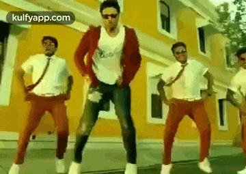 a group of men are standing in front of a yellow building dancing .