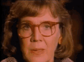 a woman wearing glasses and earrings looks at the camera