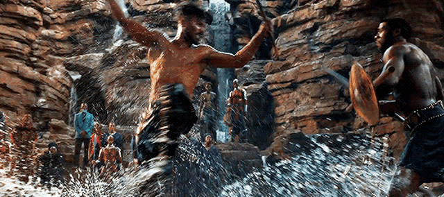 two men are fighting in the water in front of a waterfall in a cave .