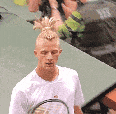 a man wearing a white wilson shirt is holding a tennis racket