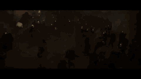 a crowd of people are standing in front of a burning building in a dark room .