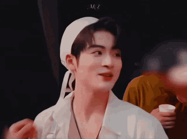 a young man wearing a white hat and a white shirt is looking at the camera .