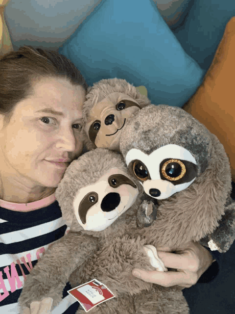 a woman is holding three stuffed sloths with a tag that says ' tiny ' on it