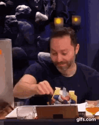 a man with a beard is sitting at a table with a tablet and a glass of beer .