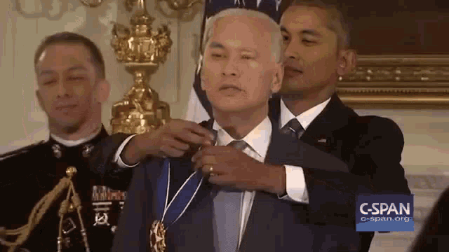 a man in a suit and tie is being pinned with a medal by a man in a black suit and tie