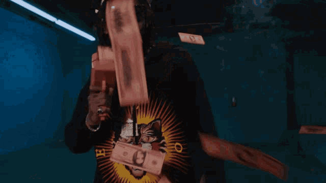 a man wearing a cat shirt is holding a cell phone in front of a bunch of money